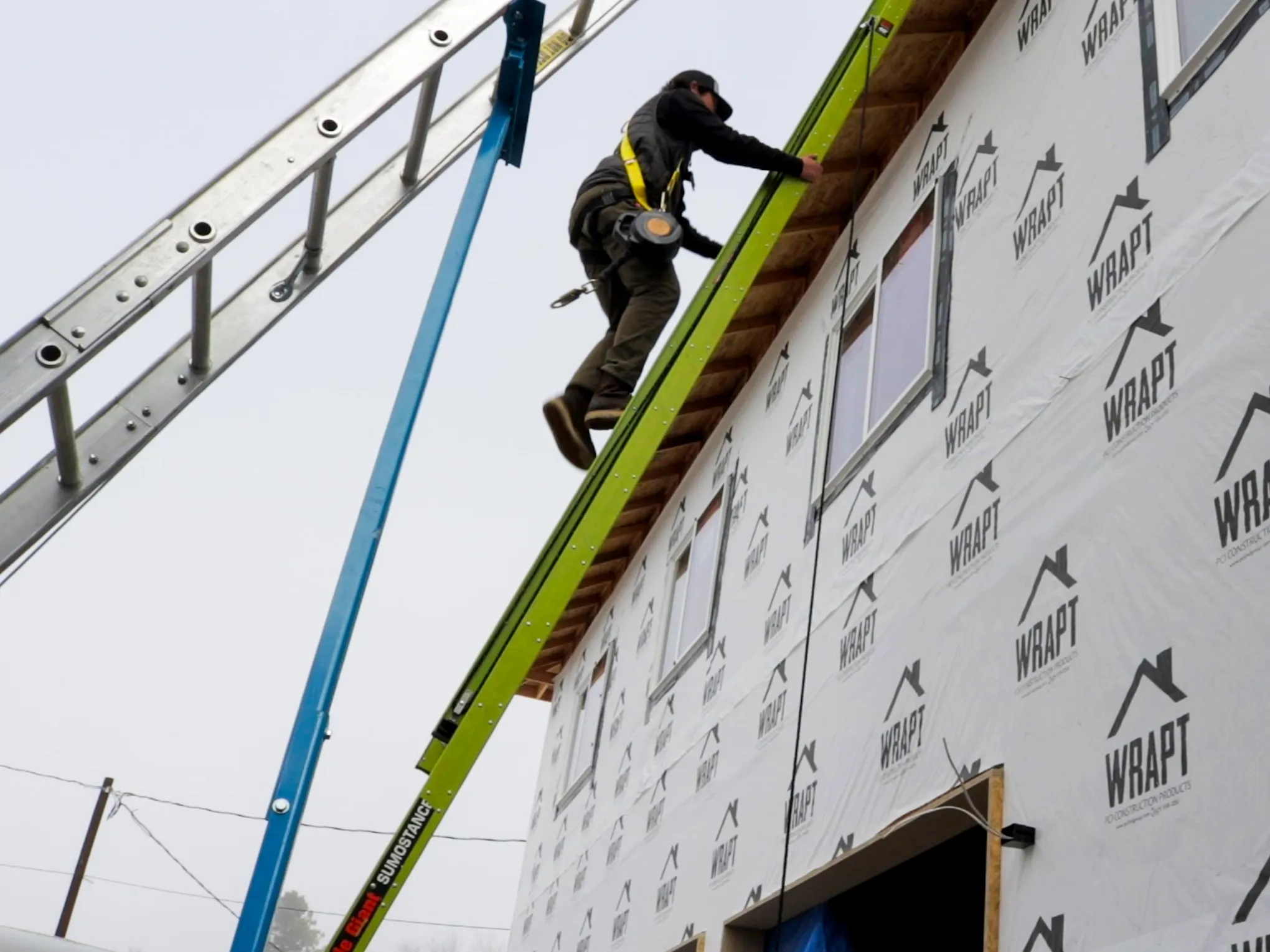 A solar installer climbing a ladder to the roof of a newly constructed home.